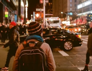 person wearing knit hat and backpack walking along the street during nighttime thumbnail