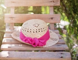 shallow focus photography of brown and pink sun hat on brown wooden chair thumbnail