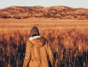 shallow focus photography of person in brown hoodie standing on brown grass field during daytime thumbnail