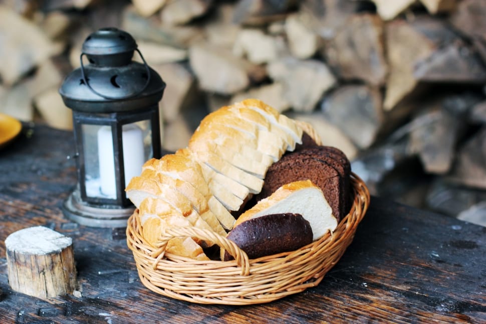 slice bread on brown wicker basket beside black candle lantern with white pillar candle on table preview