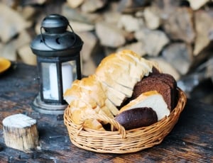 slice bread on brown wicker basket beside black candle lantern with white pillar candle on table thumbnail
