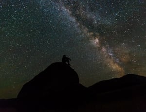man sitting on rack watching galaxy at nighttime thumbnail