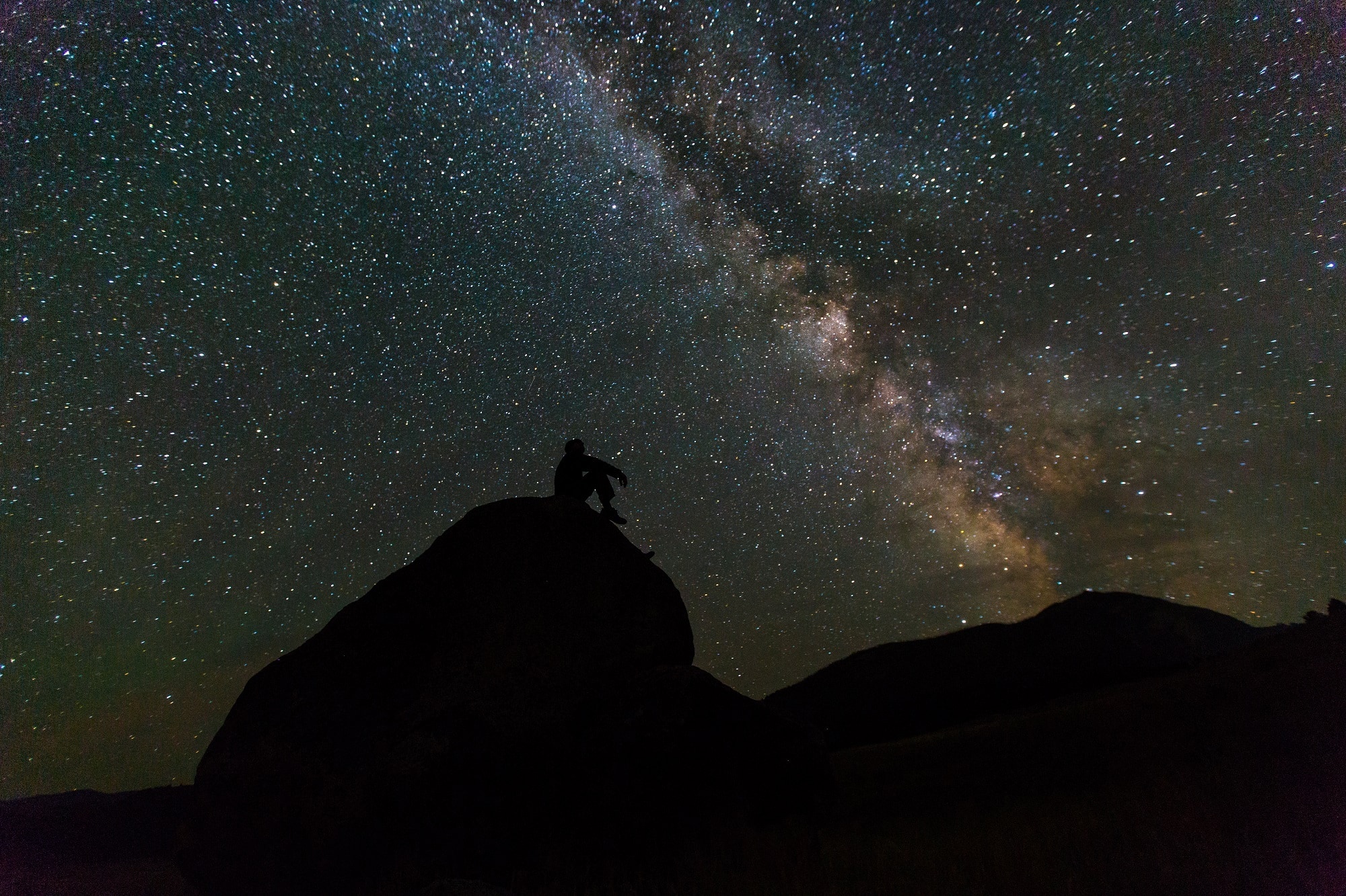 man sitting on rack watching galaxy at nighttime