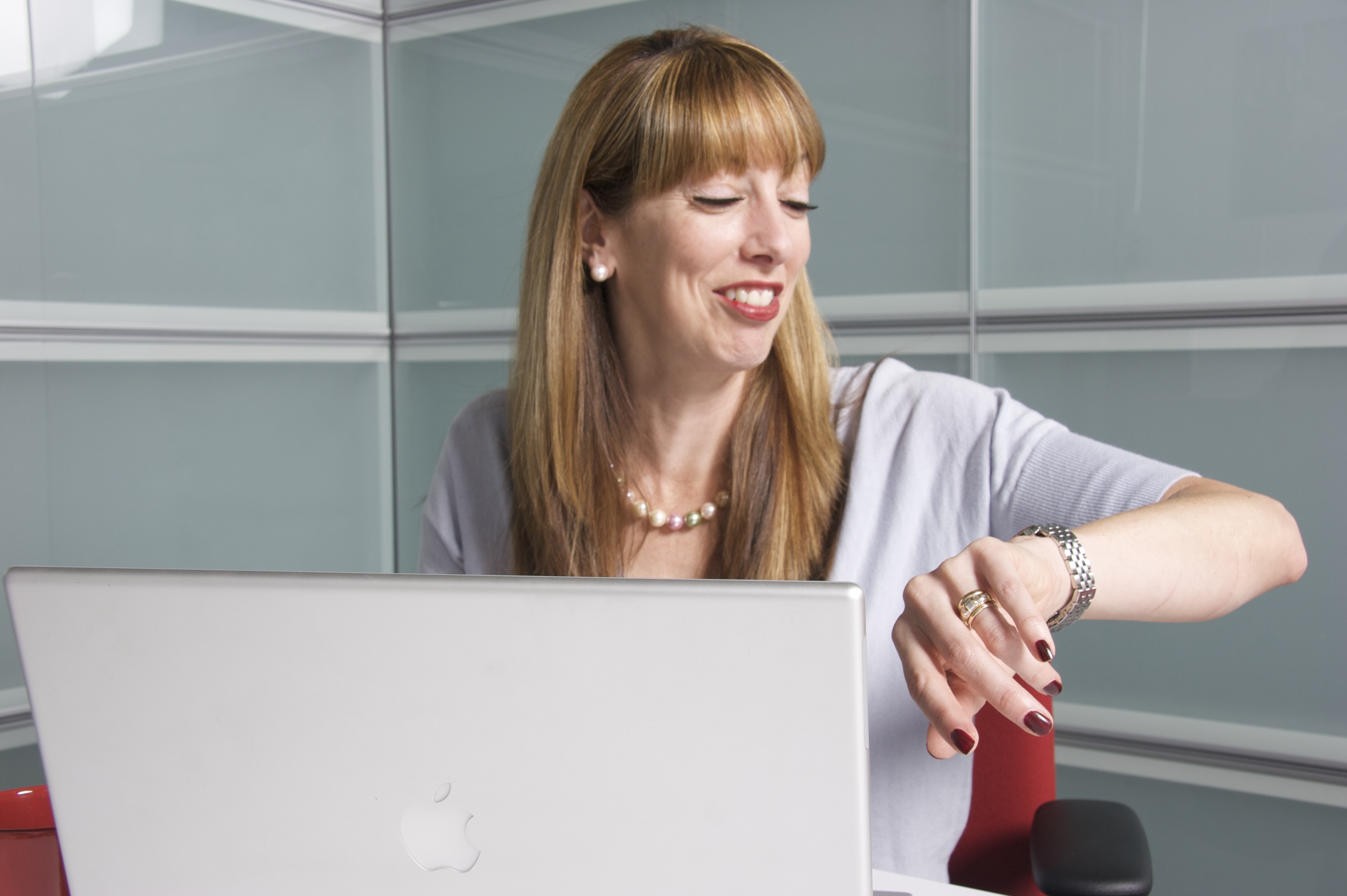 smiling woman in gray dress infront of macbook sitting on office chair