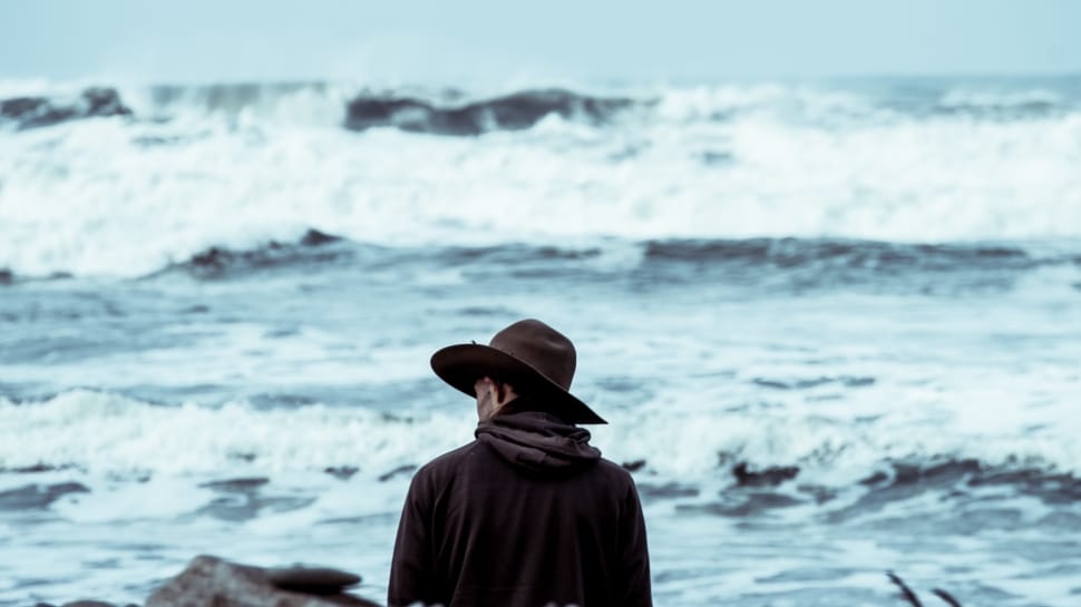 man in brown cowboy hat standing by the sea at daytime preview