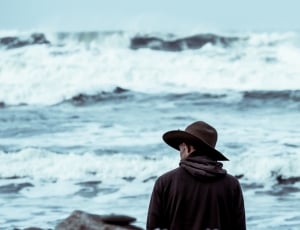 man in brown cowboy hat standing by the sea at daytime thumbnail
