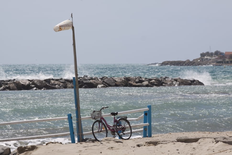 red commuter bicycle beside white and blue wooden fence on seashore during day time preview