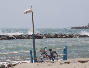red commuter bicycle beside white and blue wooden fence on seashore during day time thumbnail