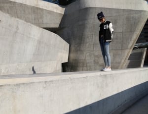 girl in letterman jacket standing on concrete railings during daytime thumbnail
