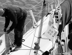 gray scale photo of man tying rope on boat thumbnail