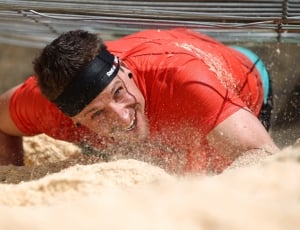 man in red crewneck shirt with black headband on sand crawling during daytime thumbnail