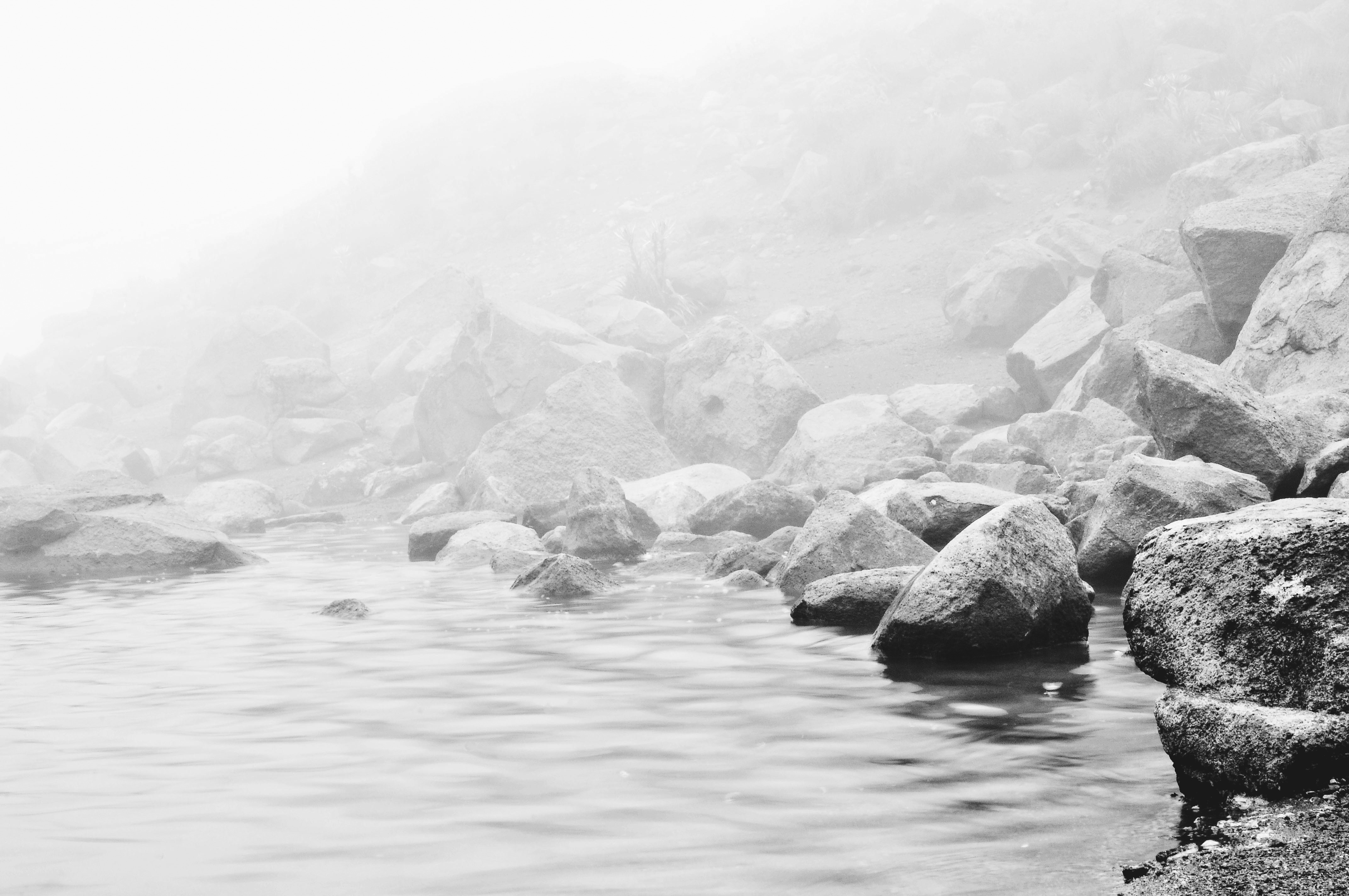 greyscale photo of rocks in body of water