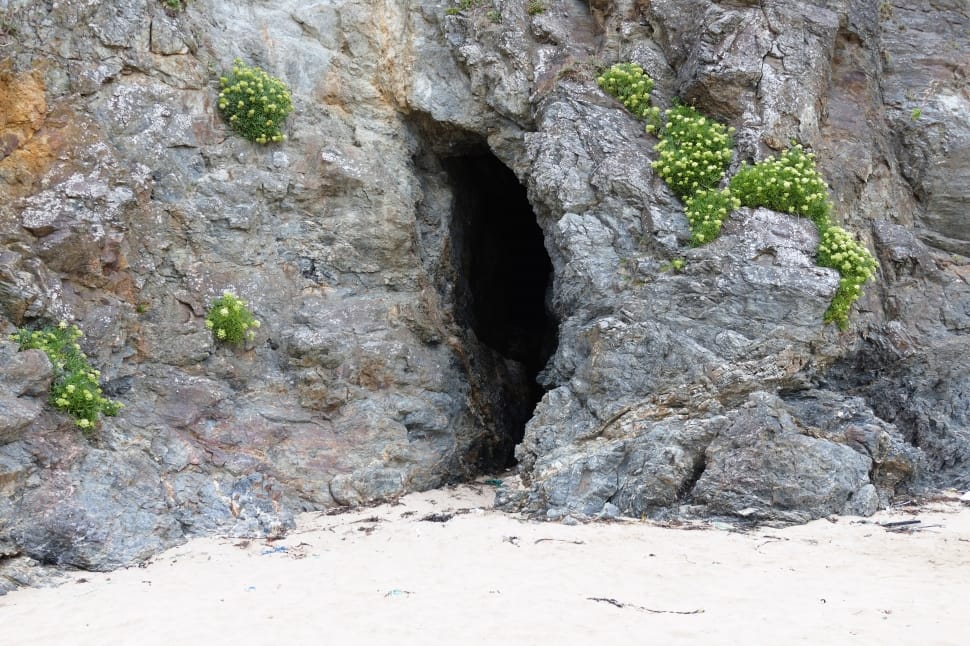 gray stone cave on white beach sand during daytime preview