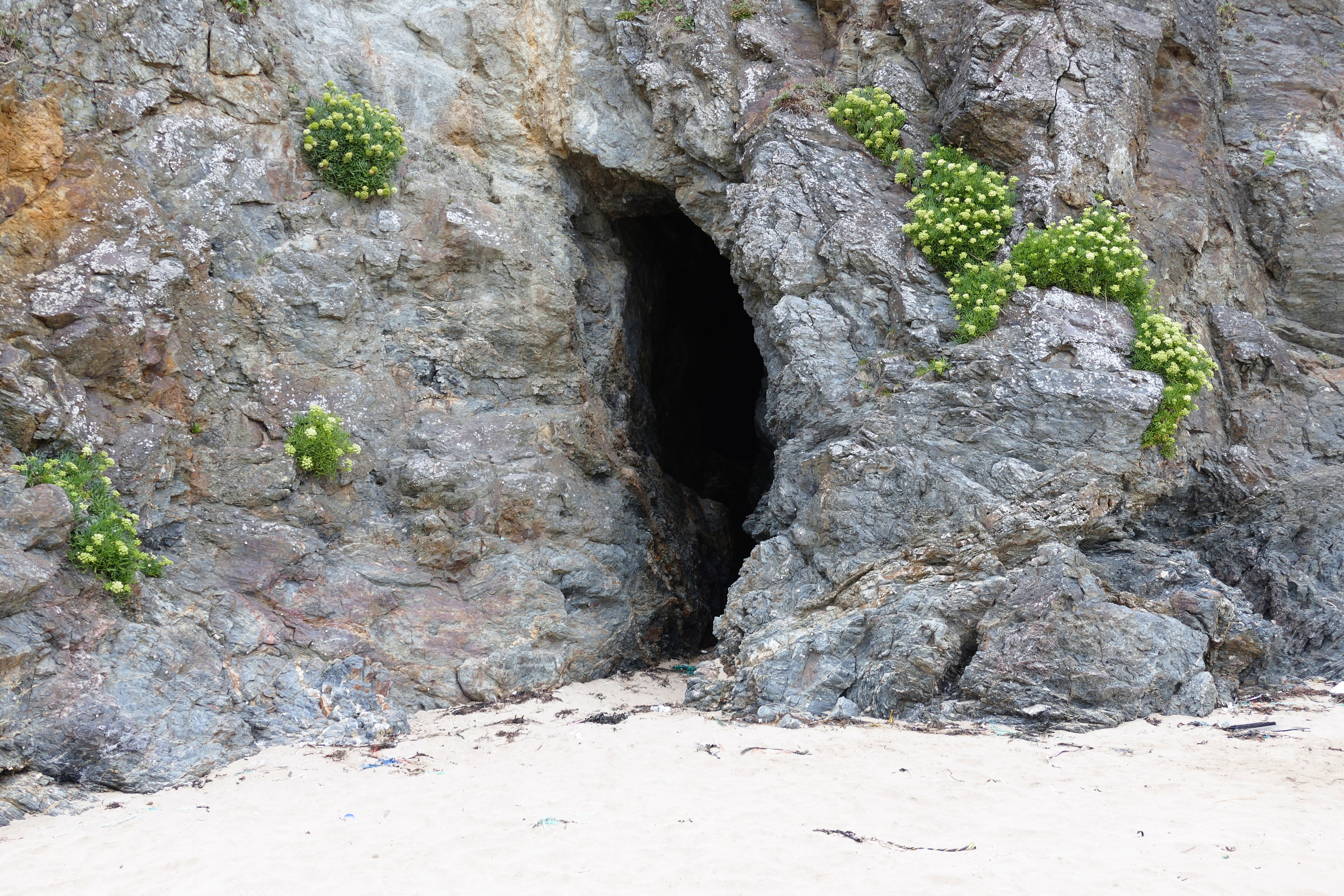 gray stone cave on white beach sand during daytime
