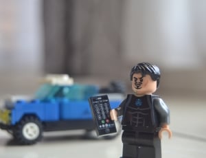 lego toy action figure holding remote next to blue lego vehicle thumbnail