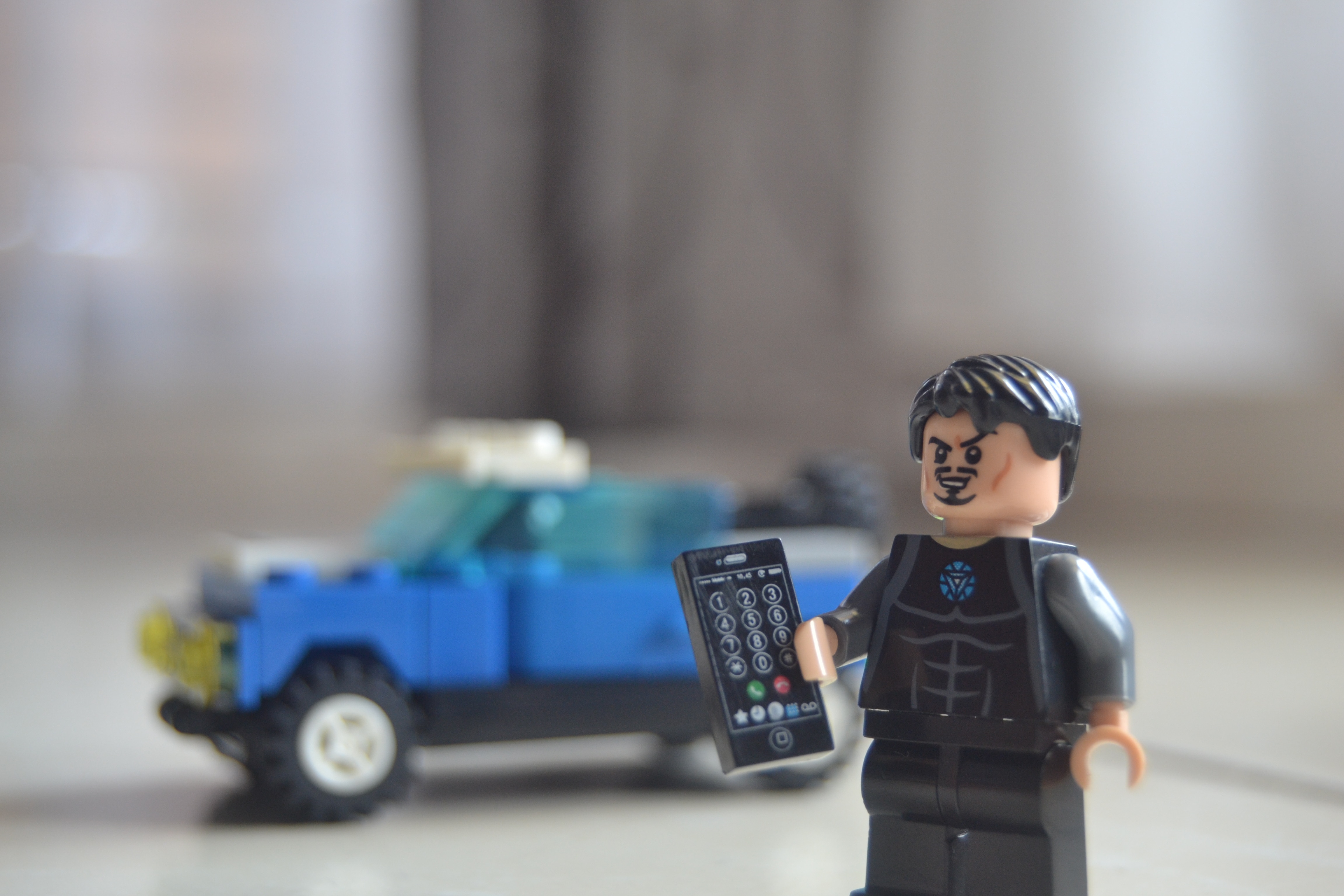 lego toy action figure holding remote next to blue lego vehicle