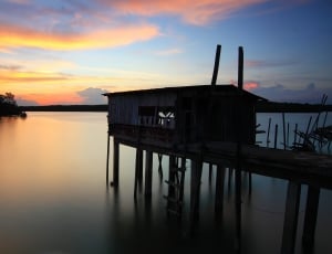 white wooden beach dock house under cloudy sky during sunset thumbnail