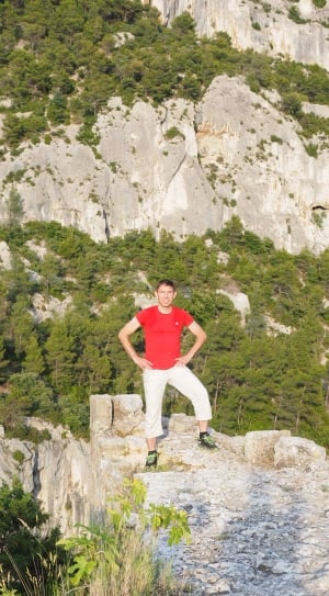 man in red shirt and white pants standing on cliff rock thumbnail