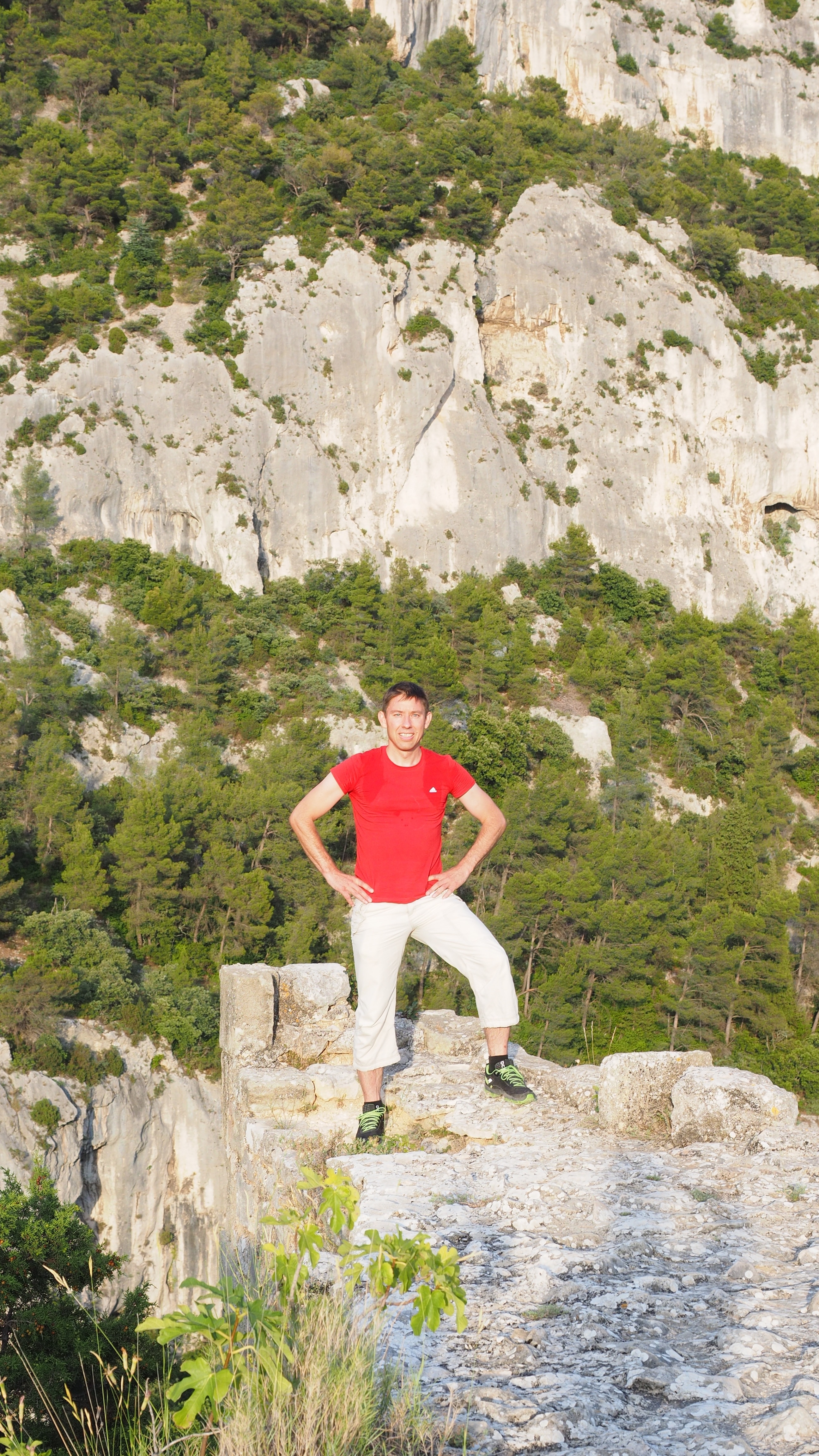 man in red shirt and white pants standing on cliff rock