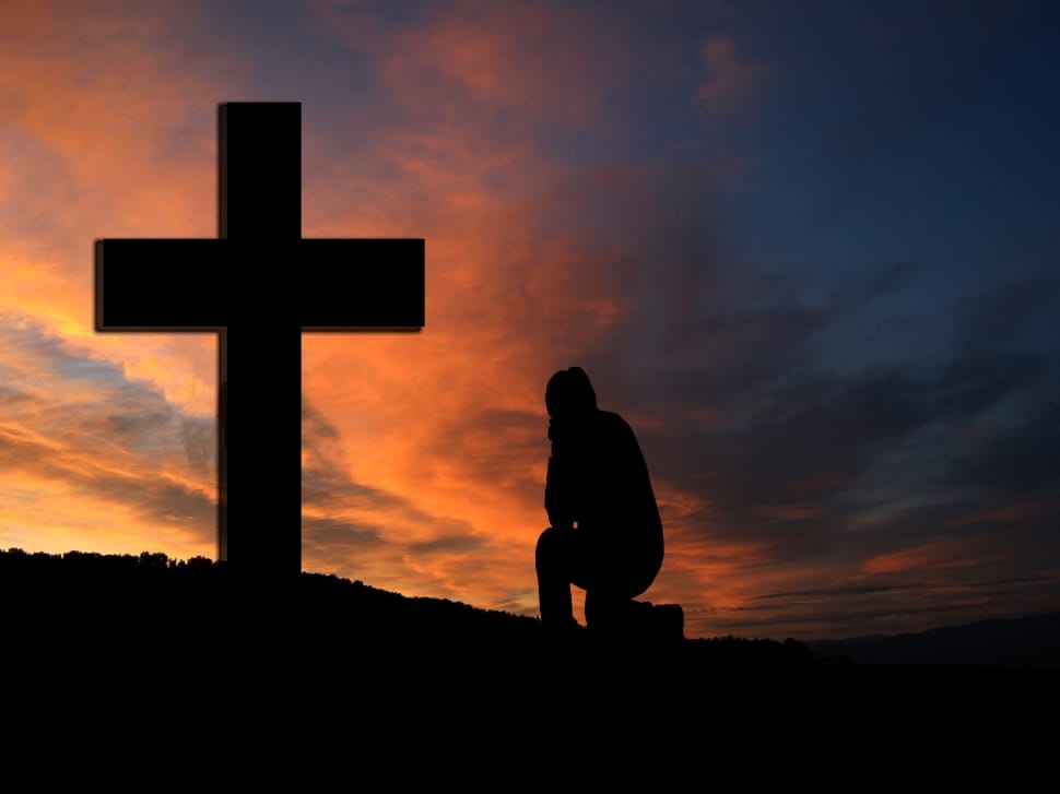 silhouette photo of person kneeling in front of cross during golden hour preview