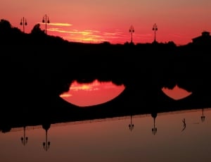 silhouette of posts reflects on water at sunset thumbnail